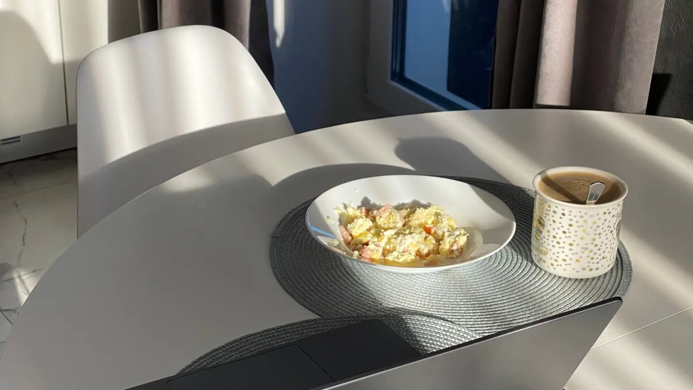 Mesa redonda del desayuno bañada por el sol, con un plato de huevos revueltos y una taza, imagen para la guía del carvedilol y la toma con alimentos